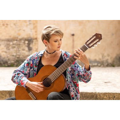 Stephanie Jones playing a CGX122MC while seated on stone steps in a courtyard of Pedraza, Segovia