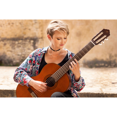 Stephanie Jones playing a CGX122MC while seated on stone steps in a courtyard of Pedraza, Spain