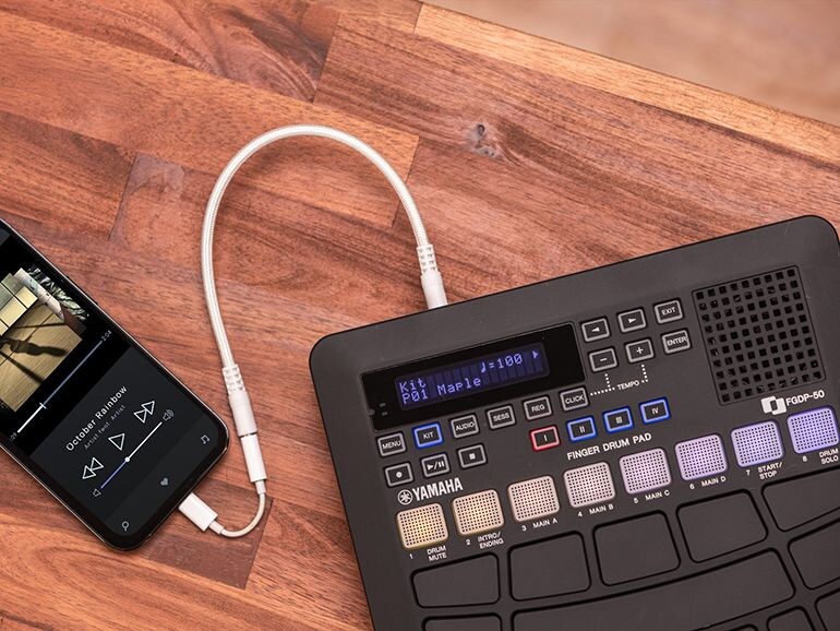 The FGDP-50 is connected to a smartphone via an audio cable. A music player app is being used on the smartphone.