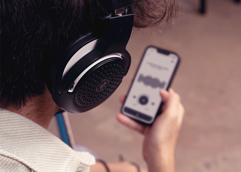 Looking over the shoulder of someone wearing YH-WL500 headphones with right hand holding a phone.