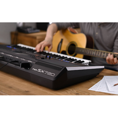 Photo of a person playing Yamaha Arranger Workstation PSR-SX720 while holding a guitar