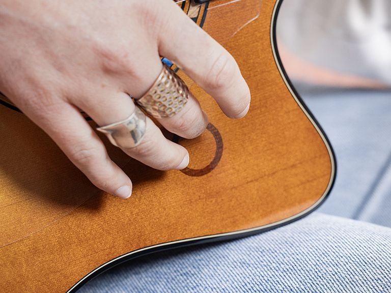 A close-up shot of the hand of a woman playing the TAG3 C and tapping the looper touch control on the guitar top.